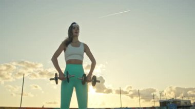 Gün batımında genç bir kadın halter kaldırıyor.