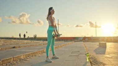 Şehir ortamında günbatımında halterleri kaldıran kadın sporcu.