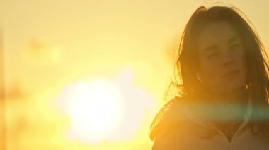 Kapalı gözlü, günbatımının tadını çıkaran dingin genç bir kadının portresi.