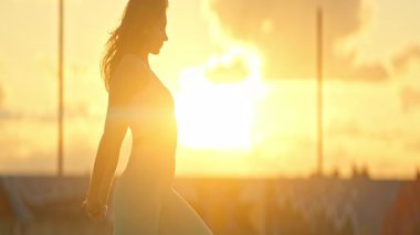 Gün batımında çatıda yoga yapan bir kadının silueti.