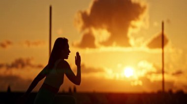 Spor kadını silueti gün batımında koşu pistinde ısınıyor.