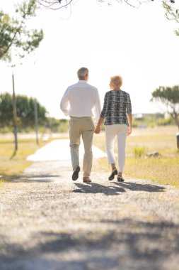 Emekli çift doğa yürüyüşünden zevk alıyor, el ele tutuşuyorlar ve çakıl yolda yürüyorlar.