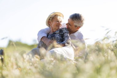 Romantik son sınıf çifti çayırda güneşli bir günün tadını çıkarıyor, kucaklaşıyor ve gülümsüyor.