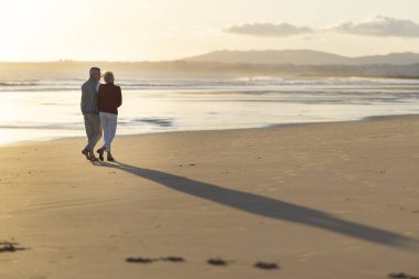 Güzel altın bir günbatımında kumsalda romantik bir yürüyüş yapan yaşlı çift.