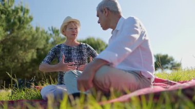 Yaşlı bir çift parkta piknik battaniyesinde otururken keyifli bir sohbet ediyor.