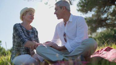 Yaşlı bir çift parkta piknik yaparken el ele tutuşup sohbet ediyorlar.