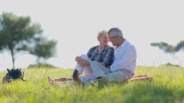Yaşlı çift güneşli bir çayırda yorganın üzerinde pikniğin tadını çıkarıyor.