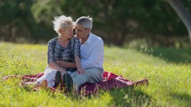 Yaşlı çift, çayır piknik battaniyesinde samimi anlar paylaşıyor.