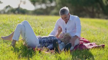 Mutlu emekli çift doğada piknik battaniyesinde birlikte vakit geçiriyorlar.