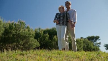 Doğada güneşli bir günün tadını çıkaran yaşlı çift el ele tutuşup gökyüzüne bakıyor.