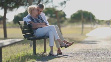 Yaşlı çift parkta rahatlatıcı bir günün tadını çıkarıyor, bankta oturuyor ve hassas anlarını paylaşıyor.