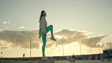 Gün batımında şehir parkında beton bir blokta atlama çalışması yapan kadın sporcu.