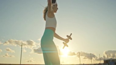 Spor kadını gün batımında dambıllarla hamle yapıyor.