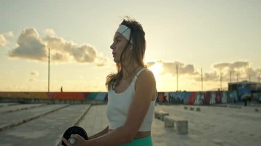 Fitness modeli şehir çatısı üzerinde altın saat boyunca dambıl egzersizleri yapar