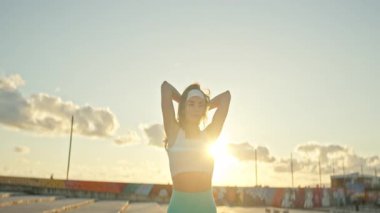 Atletik kadın gün batımı egzersizi sırasında halterle trisepsi uzatır.