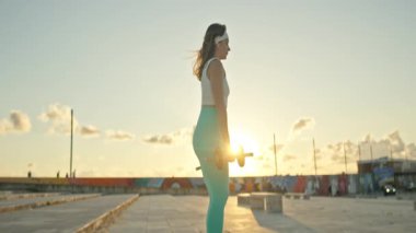 Fitness modeli gün batımında damda dambıllarla egzersiz yapıyor.