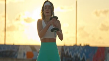 Atletik kadın günbatımında halter egzersizleri yapıyor.