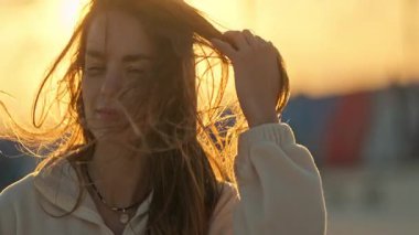 Altın saat gün batımı, kulaklık takan ve saçlarıyla oynayan genç bir kadını aydınlatıyor.
