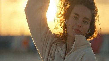 Kulaklık takan genç ve güzel bir kadın altın saat gün batımının tadını çıkarıyor.