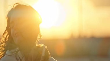 Huzurlu genç bir kadının portresi gözlerini kapatıyor ve batan güneşin sıcacık parıltısında güneşleniyor.