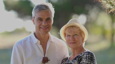 Yaşlı bir çift parkta gülümsüyor ve birbirlerine bakıyor.