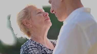 Yaşlı çift dışarıda romantik bir anın tadını çıkarıyor, burunları birbirine dokunuyor, sevgi ve bağlılık gösteriyor.