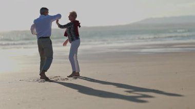 Yaşlı çift güneşli bir sahilde romantik bir dansın tadını çıkarıyor.