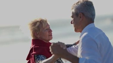 Yaşlı çift deniz kenarında romantik bir dans ediyor.