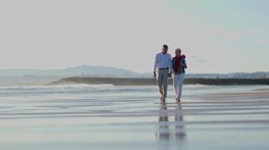 Yaşlı çift sahilde romantik bir yürüyüş yapıyor.