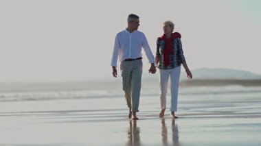 Yaşlı çift sahilde romantik bir yürüyüş yapıyor.