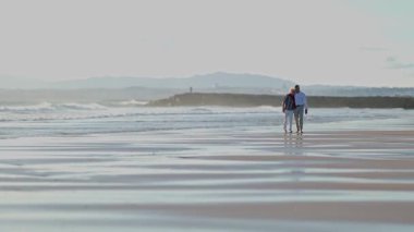 Sevecen yaşlı çift güzel bir gün batımında kumsalda rahatlatıcı bir yürüyüş yapıyor.