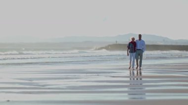 Emekli çift sahilde romantik bir yürüyüş yapıyor.