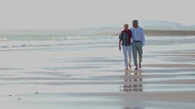Yaşlı çift sahilde romantik bir yürüyüş yapıyor.