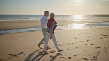 Emekli çift sahilde romantik bir yürüyüş yapıyor.