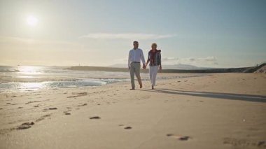 Güzel bir gün batımında kumsalda romantik bir yürüyüş yapan yaşlı çift.