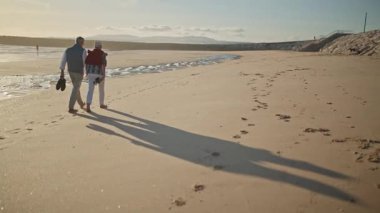 Emekli çift gün batımında sahilde romantik bir yürüyüş yapıyor.