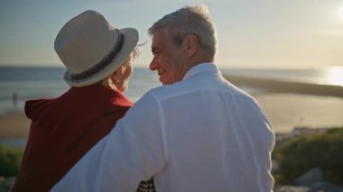 Yaşlı çift gün batımında deniz kenarında romantik bir anın tadını çıkarıyor.