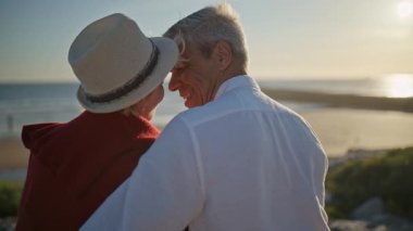 Kıdemli çift gün batımında okyanusta romantik bir anın tadını çıkarıyor.