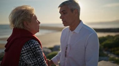 Gün batımında sahilde sohbet eden yaşlı bir çift.