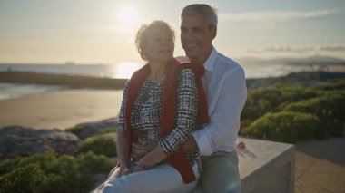 Yaşlı çift gün batımında sahilde romantik bir anın tadını çıkarıyor.