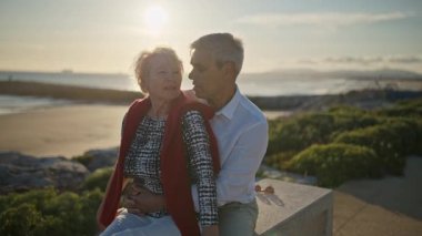 Yaşlı çift gün batımında sahilde romantik bir anın tadını çıkarıyor.