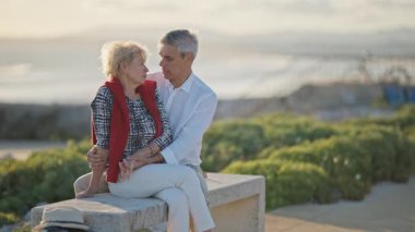 Yaşlı bir çift bankta romantik bir anın tadını çıkarıyor. Arka planda okyanus varken birbirlerinin gözlerine bakıyorlar.