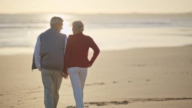 Emekli çift güzel bir gün batımında sahilde romantik bir yürüyüş yapıyor.
