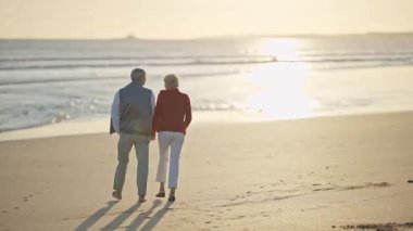 Emekli çift gün batımında sahilde romantik bir yürüyüş yapıyor.