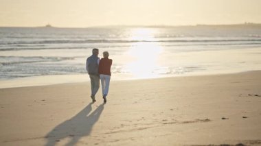 Emekli çift güzel bir gün batımında sahilde romantik bir yürüyüş yapıyor.