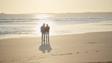 Büyük çift, altın bir günbatımında kumsalda romantik bir yürüyüş yapıyor.