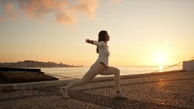 Genç bir kadın şafak vakti Lizbon 'daki tagus nehrinin orada yoga yapıyor.