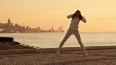 Gün doğumunda nehir kenarında esneme egzersizleri yapan genç bir kadın.