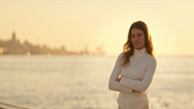 Kendine güvenen genç bir kadın kollarını kavuşturmuş Lizbon şehrinin yakınlarında altın saat güneşinin tadını çıkarıyor.