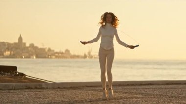 Şafakta deniz kenarında atlama ipiyle egzersiz yapan genç bir kadın.